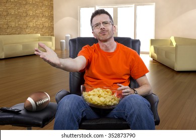 Front View Of Man Watching Football On TV With Potato Chip Snacks.  He Is A Sports Fan.