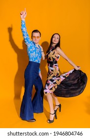 Front view of man and woman dressed in clothing like from 70s on the yellow wall isolated. Couple posing for the photoshoot. - Shutterstock ID 1946804746