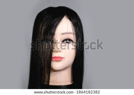 Front view of mannequin head wearing a long black wig or toupee.