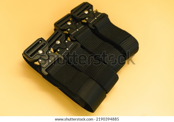 A front view of many black canvas belts with a
black fast open metal male buckle and a black belt loop lays on the
orange background. Belt. Military. Buckle. Clothing. Equipment.
Canvas. Protection