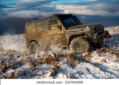 Front view of massive 4x4 off-road car on the dirty snowed ground panorama in mountains