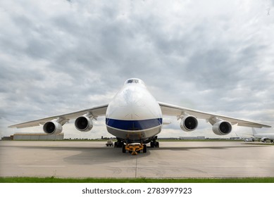 Front view massive cargo freight aircraft parked airport apron under dramatic cloudy sky. Aviation scene widebody jet powerful engines, wide wings and industrial airfreight transportation