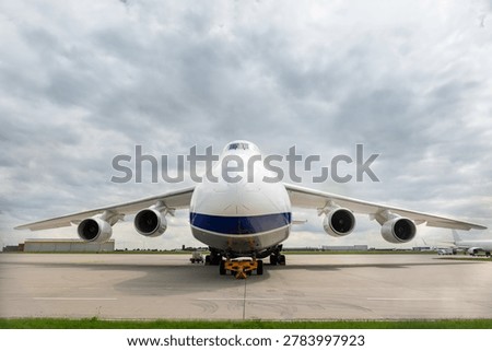 Front view massive cargo freight aircraft parked airport apron under dramatic cloudy sky. Aviation scene widebody jet powerful engines, wide wings and industrial airfreight transportation