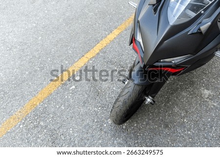Front view of a matte black and red sport motorcycle parked on the street with a gray wall background, perfect for urban automotive concepts