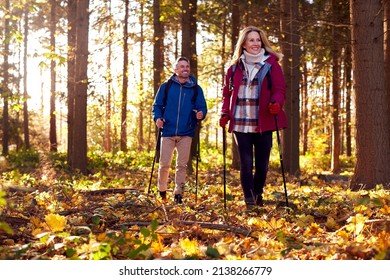 Front View Of Mature Retired Couple Walking In Fall Or Winter Countryside Using Hiking Poles