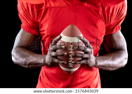 Front view mid section of an African American male American football player wearing a team uniform, pads and gloves, holding a football in his hands