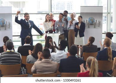 Front view of mixed race businessman standing on podium with diverse colleagues clapping as he speaks at business seminar in office building - Shutterstock ID 1330493261