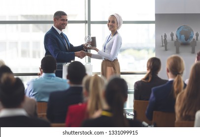 Front view of mixed race businesswoman receiving award from mixed race businessman in front of business professionals sitting at a business seminar in office building - Powered by Shutterstock