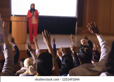 Front View Of Mixed Race Businesswoman Standing Around The Podium In The Auditorium While Audience Raising Hand For Asking Question 