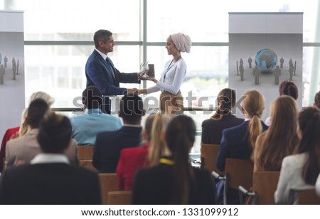 Front view of mixed race businesswoman receiving award from black businessman at business seminar in office building