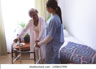 Front View Of Mixed Race Female Nurse Helping Senior African American Female Patient To Stand With Walker At Nursing Home