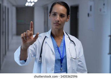 Front view of Mixed-race female doctor pretending to touch an invisible screen in the corridor at hospital - Powered by Shutterstock