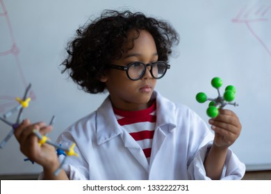 Front view of a Mixed-race  schoolboy holding and examining different molecule model while standing in front of the white board in the laboratory at school - Powered by Shutterstock