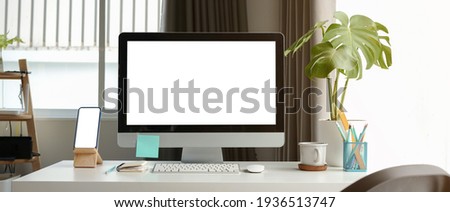 Front view of mock up computer and smart phone with blank screen on white table at contemporary workplace.