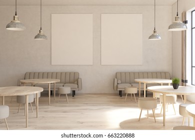 Front view of a modern cafe interior with two vertical posters on a concrete wall, wooden floor, round tables and chairs and beige sofas near tall windows. 3d rendering mock up