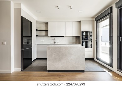 Vista frontal de una moderna cocina de diseño con armarios lisos y sin mango con bordes negros, electrodomésticos de cristal negro, una isla de mármol y encimeras de mármol