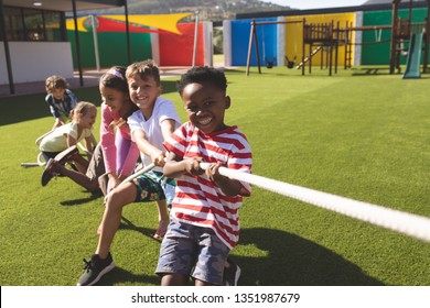 Front View Of Multi Ethnic Group Of Happy School Kids Playing Tug Of War In Playground