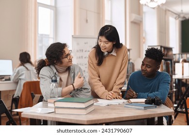 Front view at multiethnic group of three students studying together around table in college library with focus on young Asian woman - Powered by Shutterstock