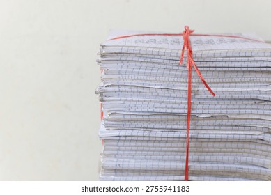 A front view of multiple stacks of old school notebooks and colorful books, securely tied with red and blue plastic ropes, ready for recycling or storage.