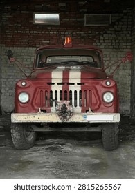 Front view of old red fire truck parked inside dark brick garage on concrete floor, concept of vintage emergency rescue equipment
