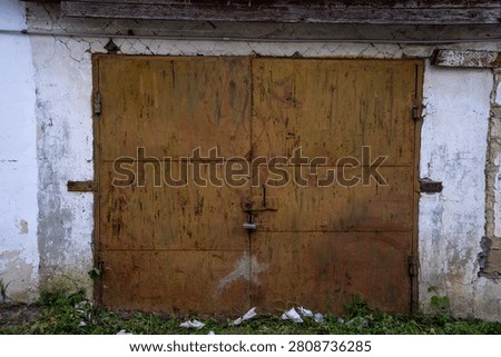 Front view of old rusty iron garage doors closed with a padlock on a weathered concrete wall background.