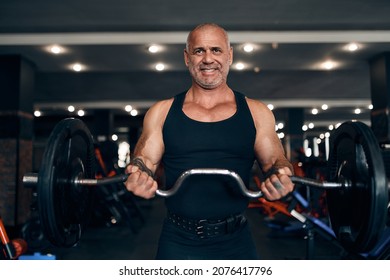  Front View Of Older Muscular Bald Caucasian Man Working Out In Gym Doing Exercises With Barbell At Biceps. Bodybuilding Concept 