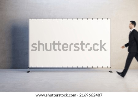 Front view on blank white billboard with place for your text or logo and walking man in black suit on concrete wall background, mock up