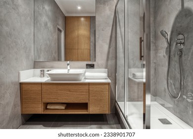 front view on ceramic washbasin with water tap, clean towel folded on white countertop, wooden under sink cabinet and vanity mirror on wall at bathroom with modern interior design