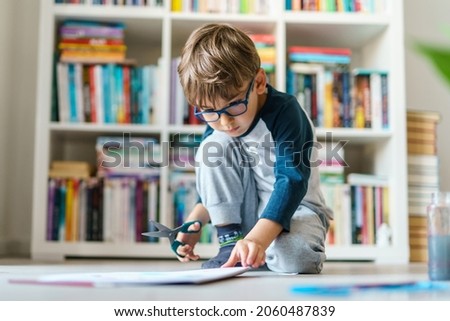 Front view on four years old caucasian boy playing n the floor at home - little kid using scissors to cut paper education developing art skills growing up concept