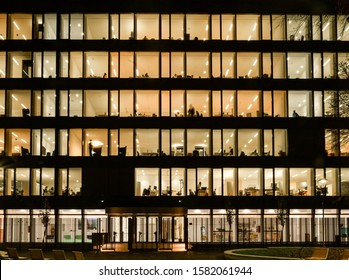 Front View On Illuminated Offices Of A Corporate Building With People Working Overtime. Long Exposure At Night.