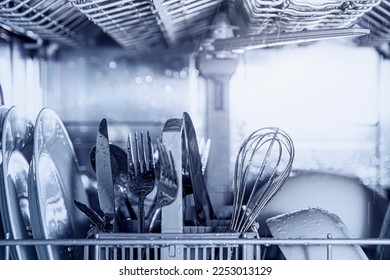Front view of open automatic stainless steel built-in fully integrated top control dishwasher range machine with clean utensils, cutlery, glasses, dishes, plates inside in modern home kitchen