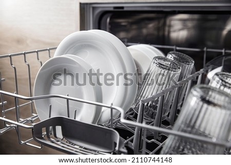 Front view of open automatic stainless fully integrated dishwasher range machine with clean utensils, cutlery, inside at modern home kitchen. Household domestic, kitchen appliances, lifestyle view