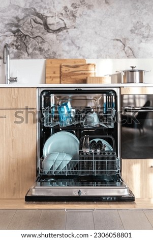 Front view of open dishwasher with pull-out shelves. Clean, dry blue plates, mugs, spoons and forks. Modern kitchen with easy to use appliances. Save water and energy efficient home equipment concept