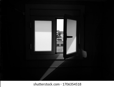 Front view of an open window, light enters through it and in the background you can see buildings. Abstract background image. Conceptual black and white photography. Concept of light and darkness.