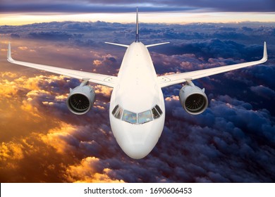 Front view of the passenger plane in flight. Aircraft fies high over the clouds during sunset.