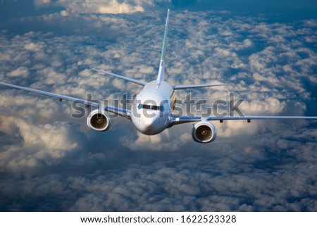 Front view of a passenger plane flying above the clouds. White passenger aircraft in flight during sunset.
