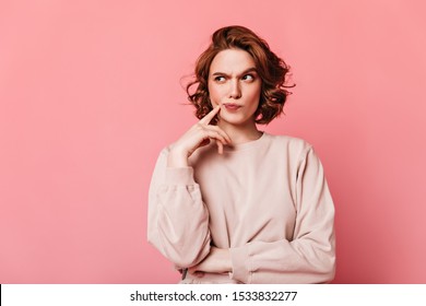 Front view of pensive pretty woman. Curly girl thinking on pink background.