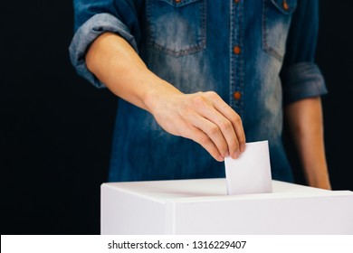 Front view of person holding ballot paper casting vote at a polling station for election vote in black background