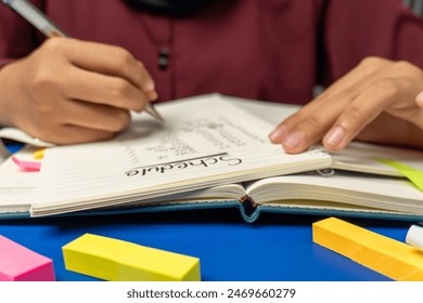 front view of person writing a daily activity schedule in a notebook on table - Powered by Shutterstock