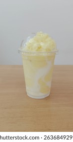 front view pineapple smoothie in a plastic cup placed on a wooden floor, white wall background, food, drink, health, copy space