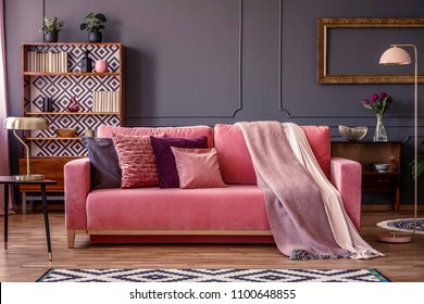 Front view of a pink sofa with pillows and blanket, vintage cupboard in the background in a glamorous living room interior