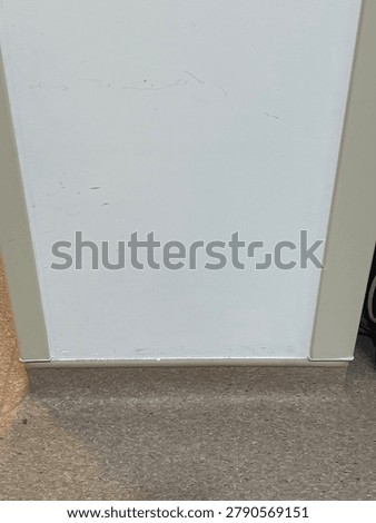 Front view of a plain white interior wall with scuff marks, bounded by corner guards and a brown baseboard floor line.
