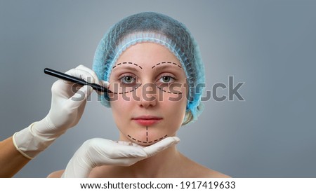 Front view of a plastic surgeon drawing lines on a face of young woman prior to cosmetic surgery. Concept of visage improvement and beauty healthcare in clinic.