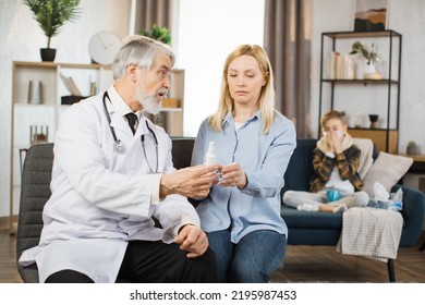 Front View Of Pleasant Confident Mature Male Doctor , Talking With Concentrated Pretty Caucasian Woman About Taking Of Medicines During Home Visit Of Sick Boy.