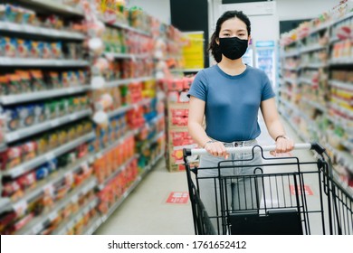 Front View Portrait Of Asian Young Woman Wear A Black Face Mask For Prevent Virus Are Holding A Cart Between Aisle At Supermarket, New Safety Shopping Lifestyle Concept With Copy Space