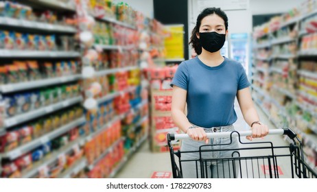 Front View Portrait Of Asian Young Woman Wear A Black Face Mask For Prevent Virus Are Holding A Cart Between Aisle At Supermarket, New Safety Shopping Lifestyle Concept With Copy Space