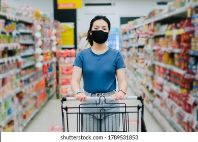 Front View Portrait Of Asian Young Woman Wear A Black Face Mask For Prevent Virus Are Holding A Cart Between Aisle At Supermarket, New Safety Shopping Lifestyle Concept With Copy Space