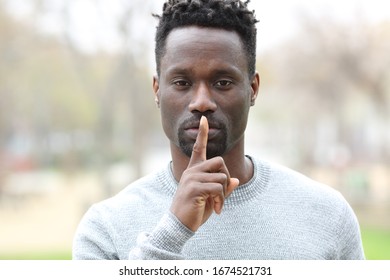 Front View Portrait Of A Black Man Asking For Silence With Finger On Lips Standing In A Park