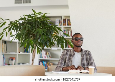 Front view portrait of blind African-American man reading Braille book in library, copy space