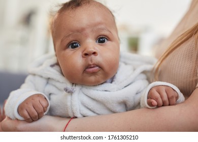 Front view portrait of cute African-American baby looking at camera while lying in mothers arms